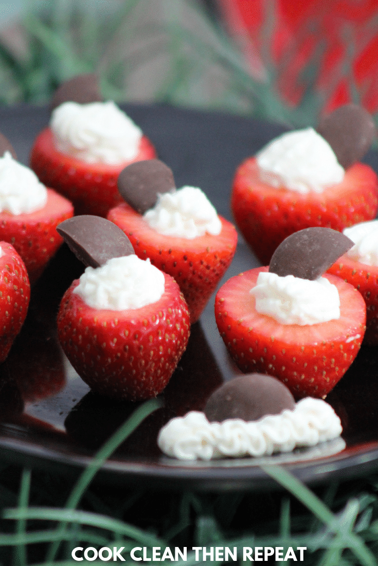 Tall image that shows the strawberries on a black plate with some fake grassy strands in front and back.