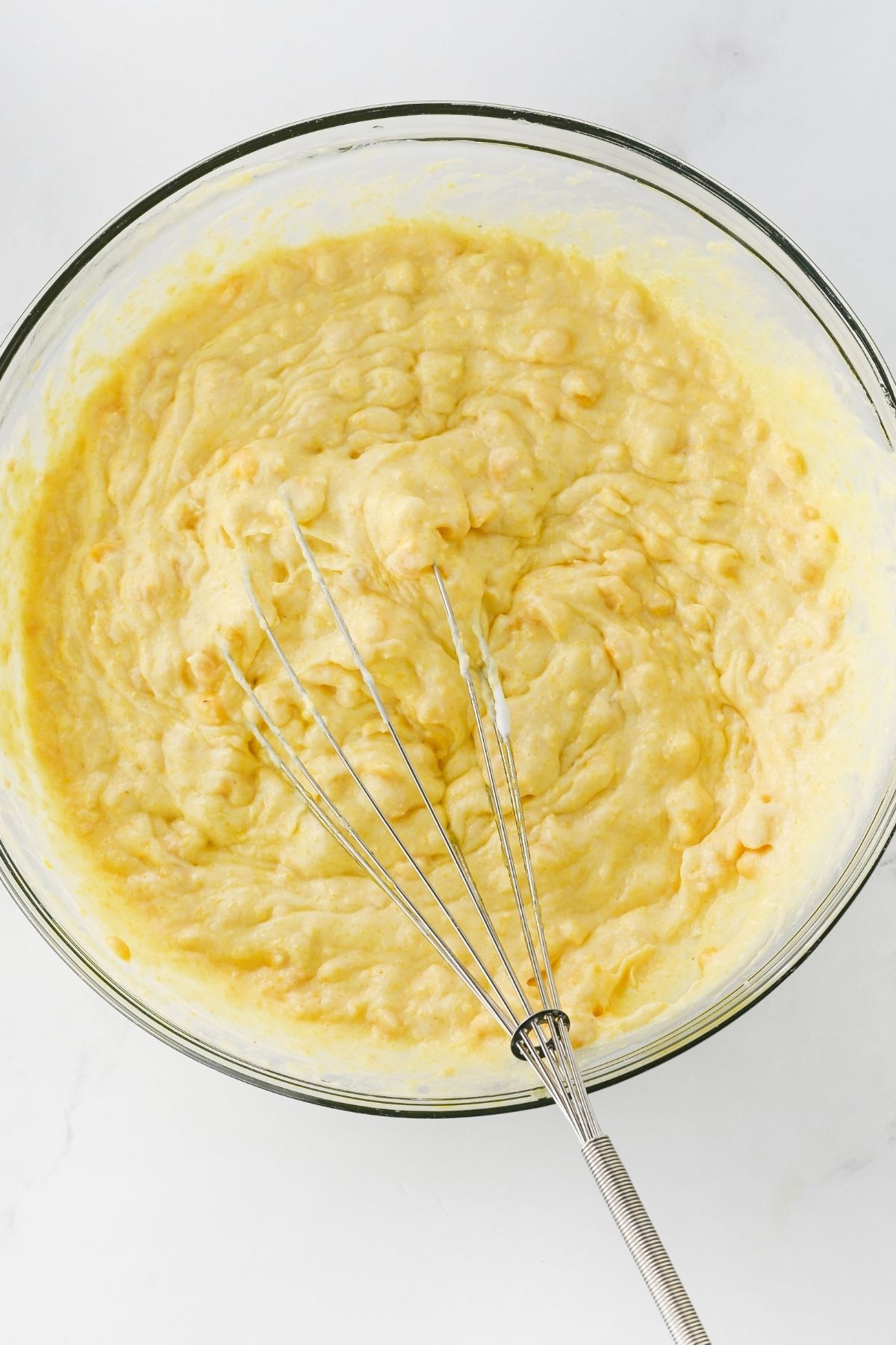 Cornbread casserole being mixed in a glass mixing bowl.