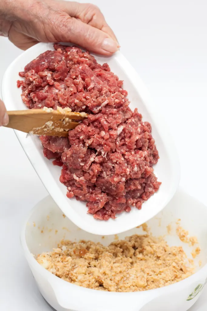 Spooning ground meat until a white bowl of bread crumbs.