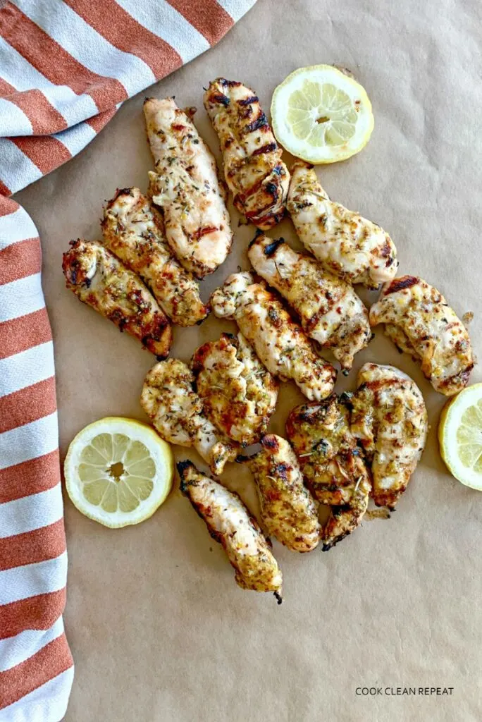 Grilled chicken tenders on parchment paper with sliced lemons. 