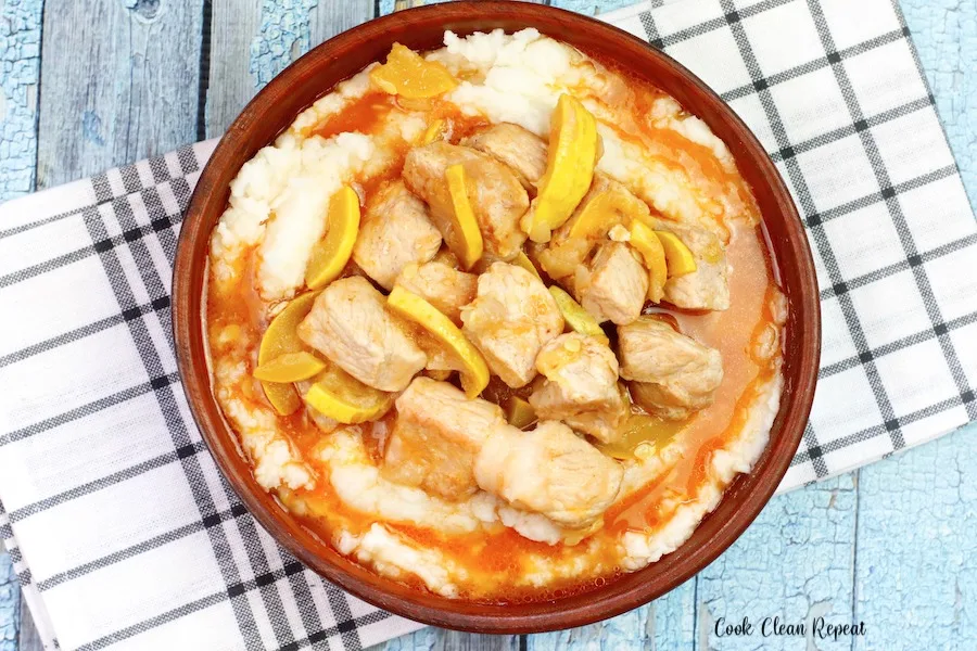 A top down look at a bowl with a serving of pork and squash over mashed potatoes. 