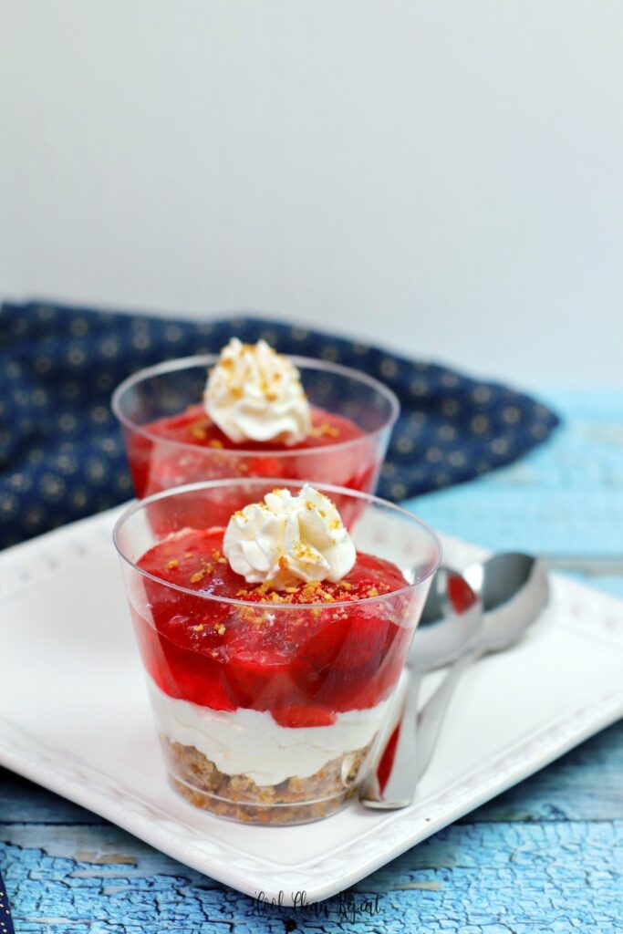 Two strawberry jello salad with cool whip cups ready to be eaten on a plate with a spoon. 