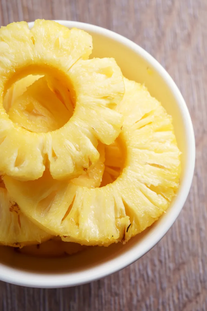 Fresh pineapple rings in a white bowl on a wooden background. 