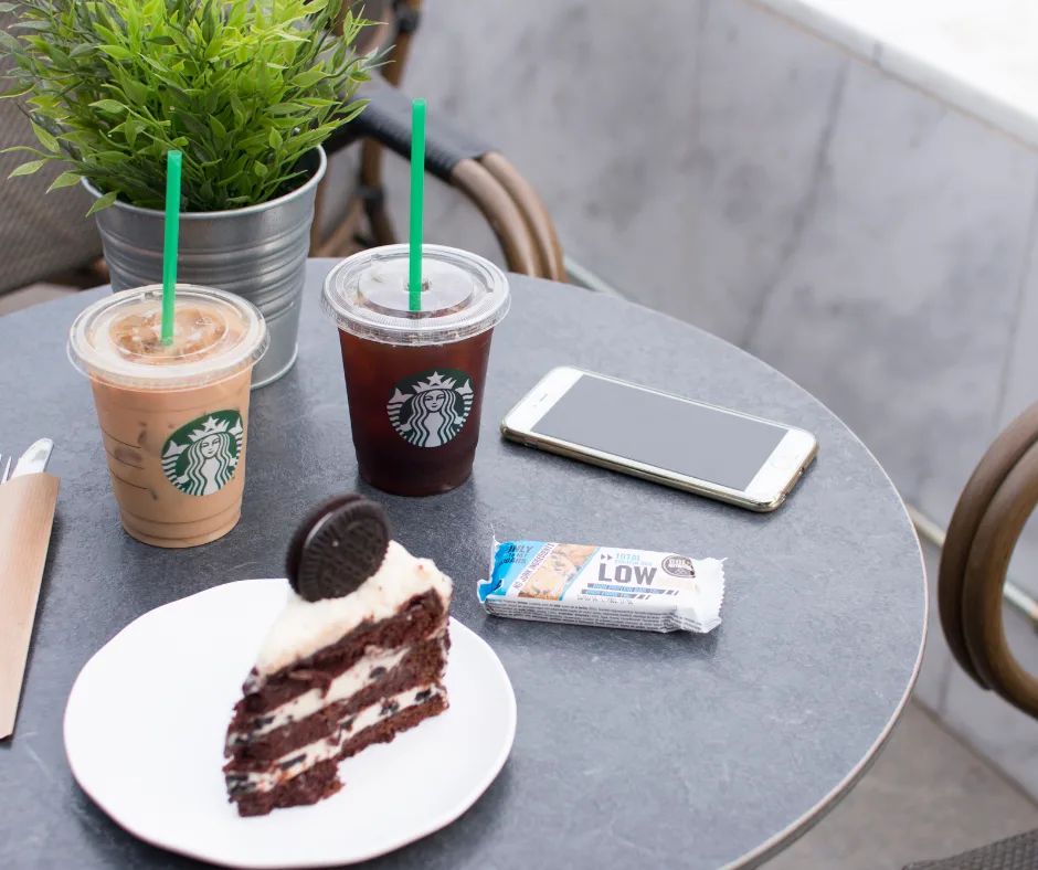 Some Starbucks coffee drinks with cake on a table by a phone. 