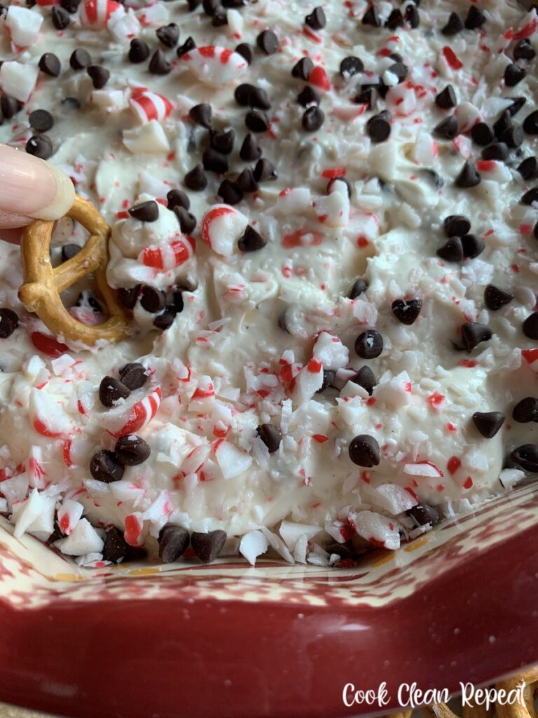 A pretzel being dipped in to the candy cane cheesecake dip ready to share. 