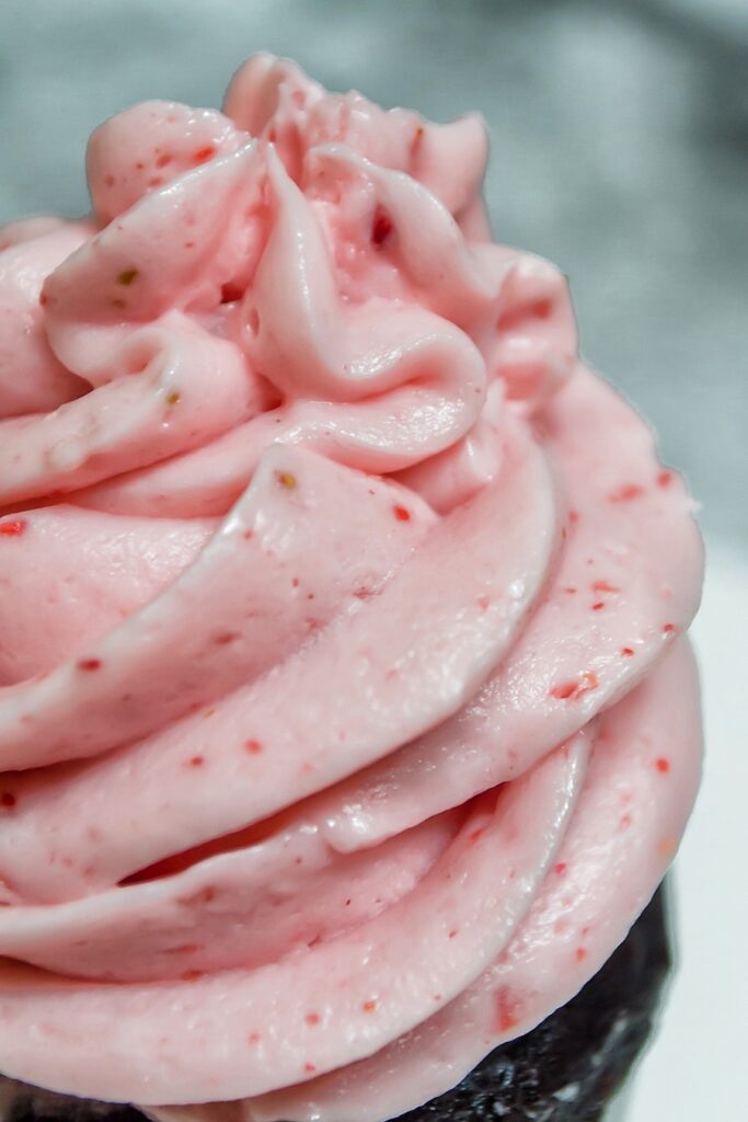 A big pile of strawberry icing on top of a cupcake. 