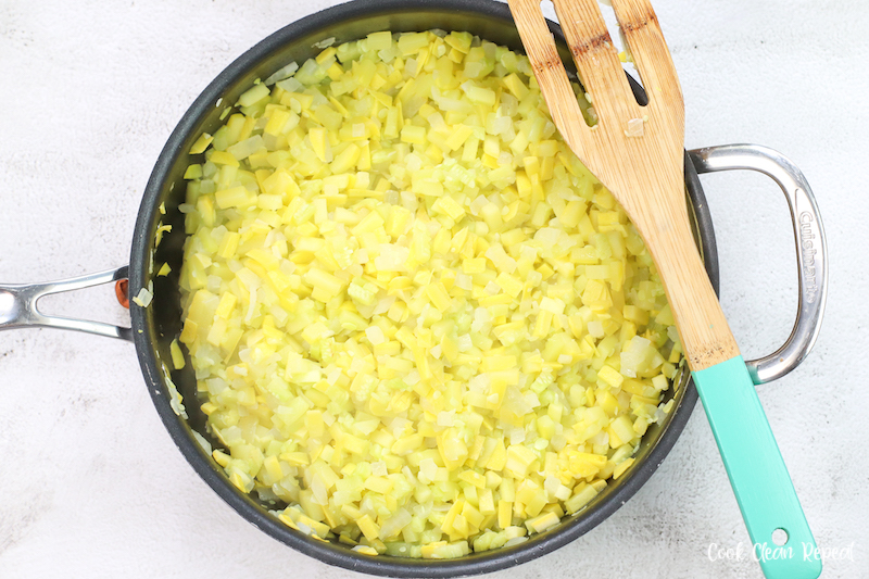 sauted yellow squash and onion in a frying pan with a wooden spatula. 