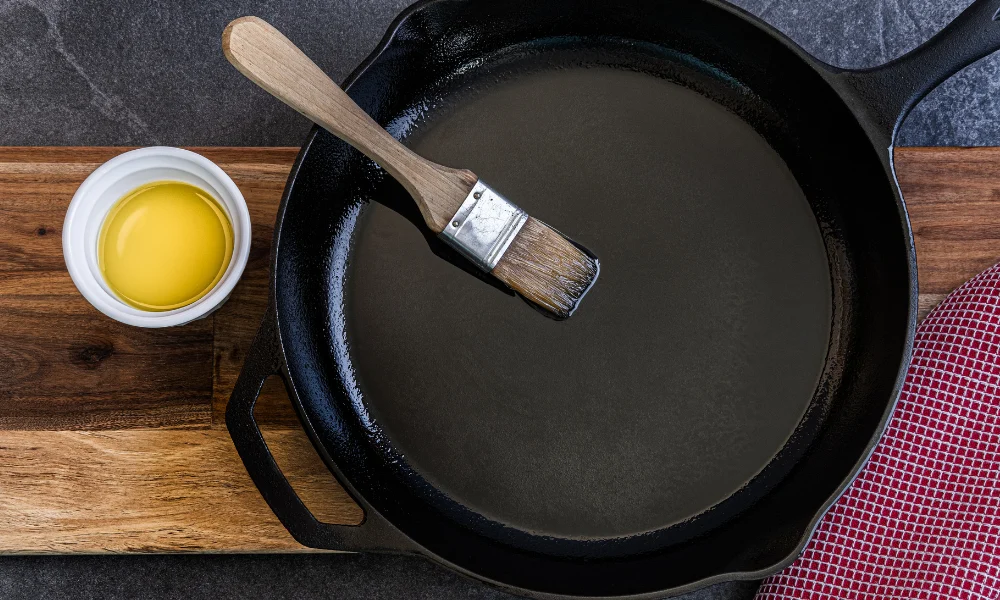 brushing a cast iron skillet with oil on a butcher block top.