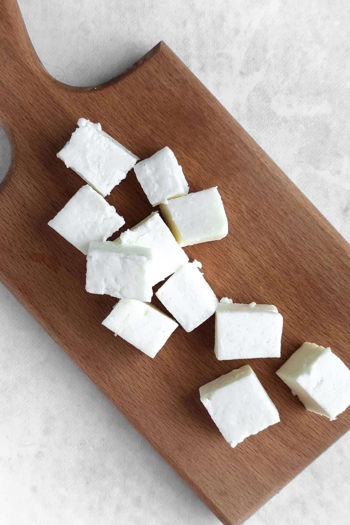 Cubes of feta cheese sitting on a wooden cutting board.