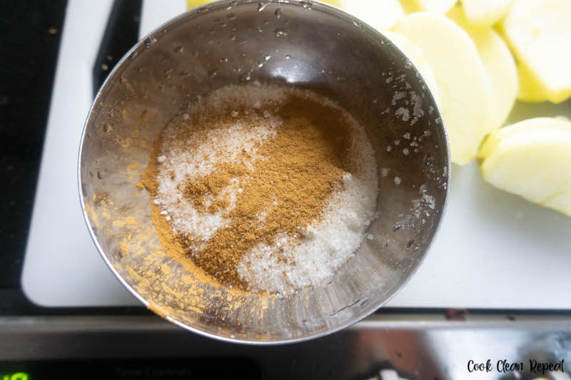 Cinnamon and sugar being mixed together in a large stainless steel mixing bowl. 