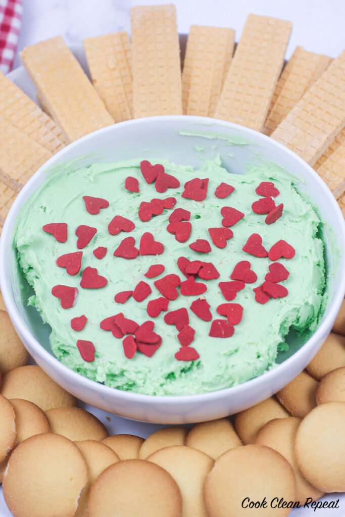 a bowl full of the finished grinch dip ready to eat with cookies and pretzels. 