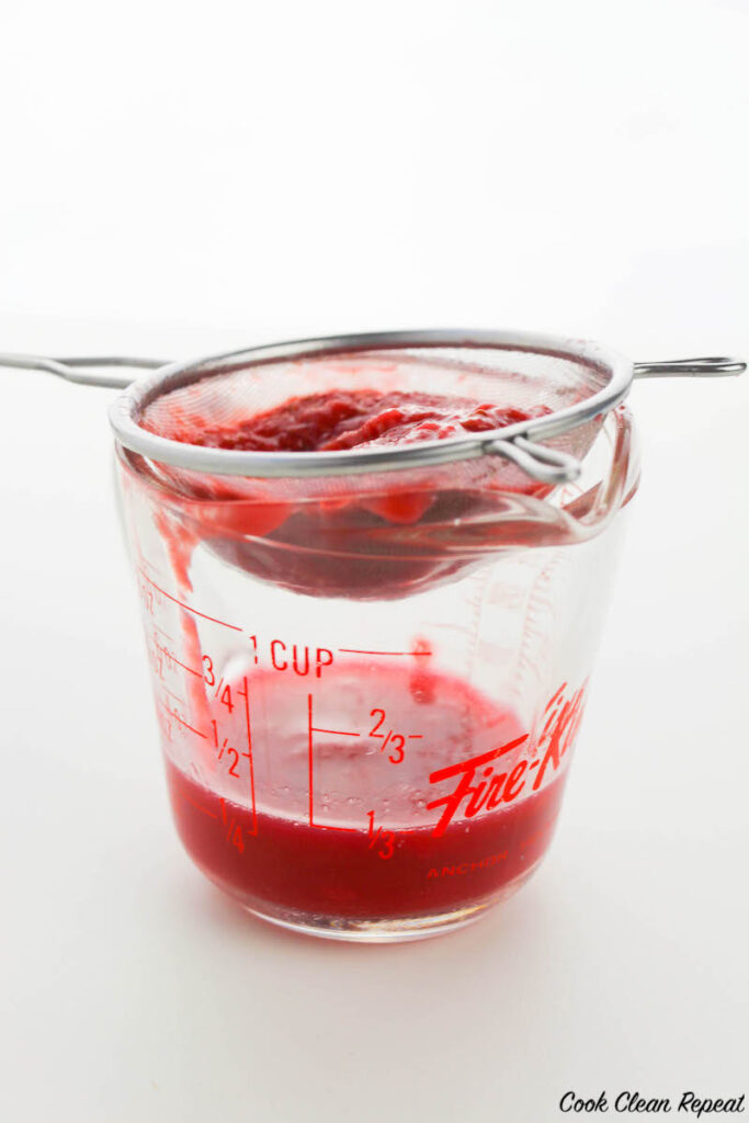 raspberry syrup being strained into a glass measuring cup
