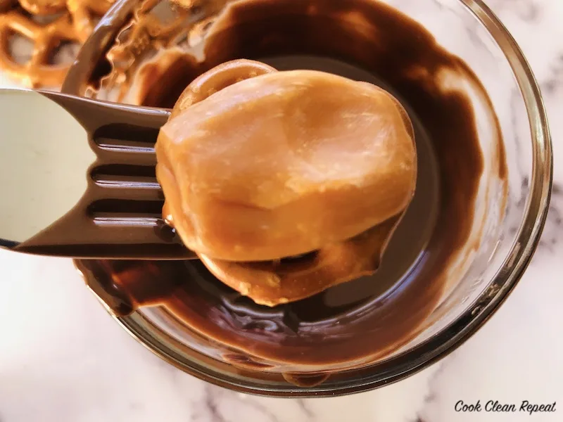 dunking the caramel and pretzel into the chocolate. 