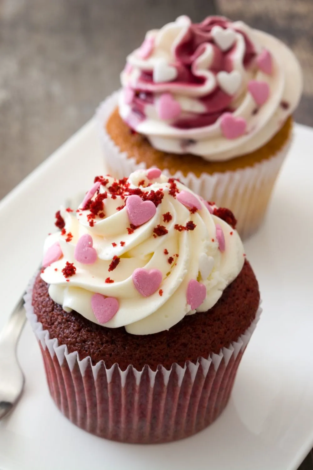 two cupcakes on a plate with valentines hearts on the icing