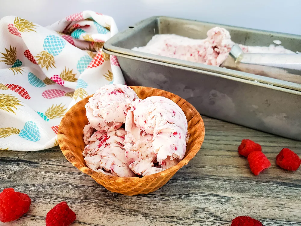 Scoops of no churn raspberry ice cream served in a waffle bowl with the rest of the ice cream in the mold in the background.