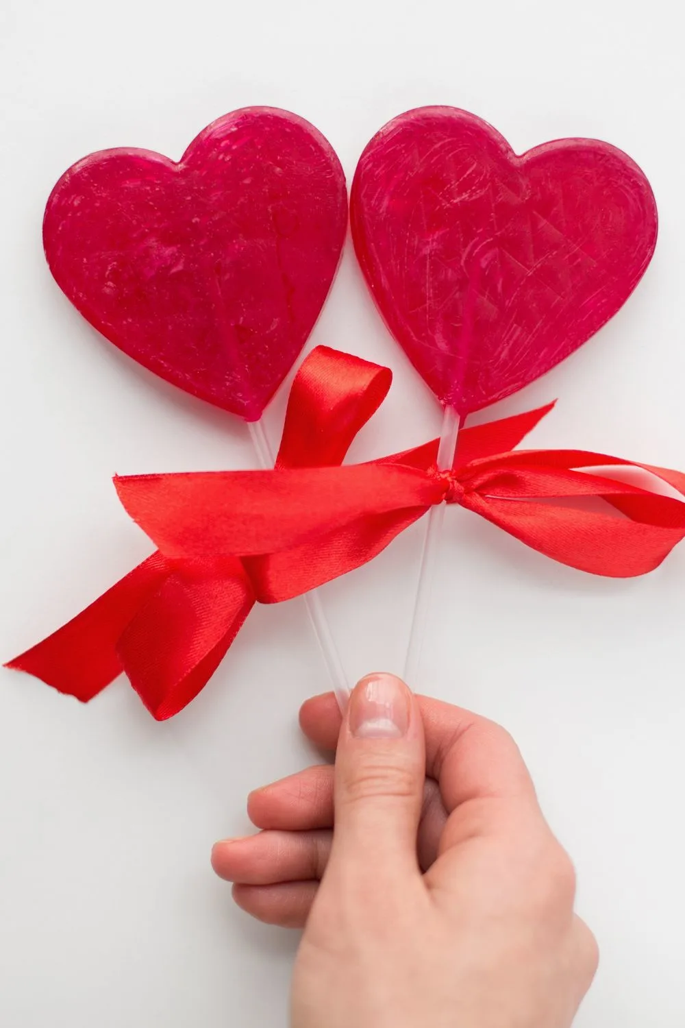 someone holding two heart shaped lollipops