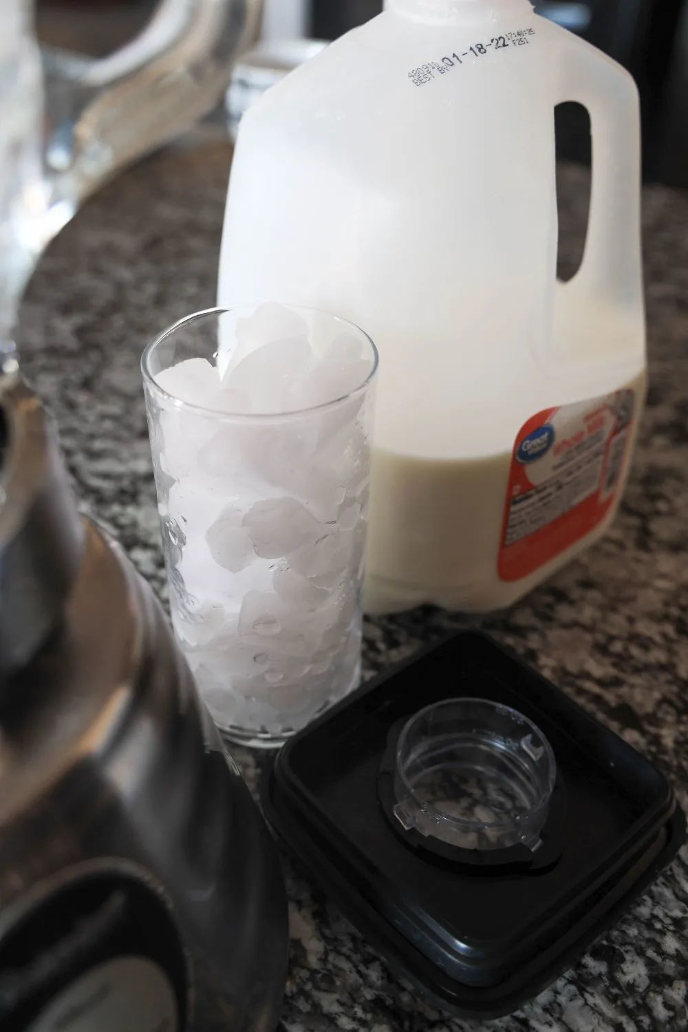 ice cubes in a glass beside a blender and a jug of milk.