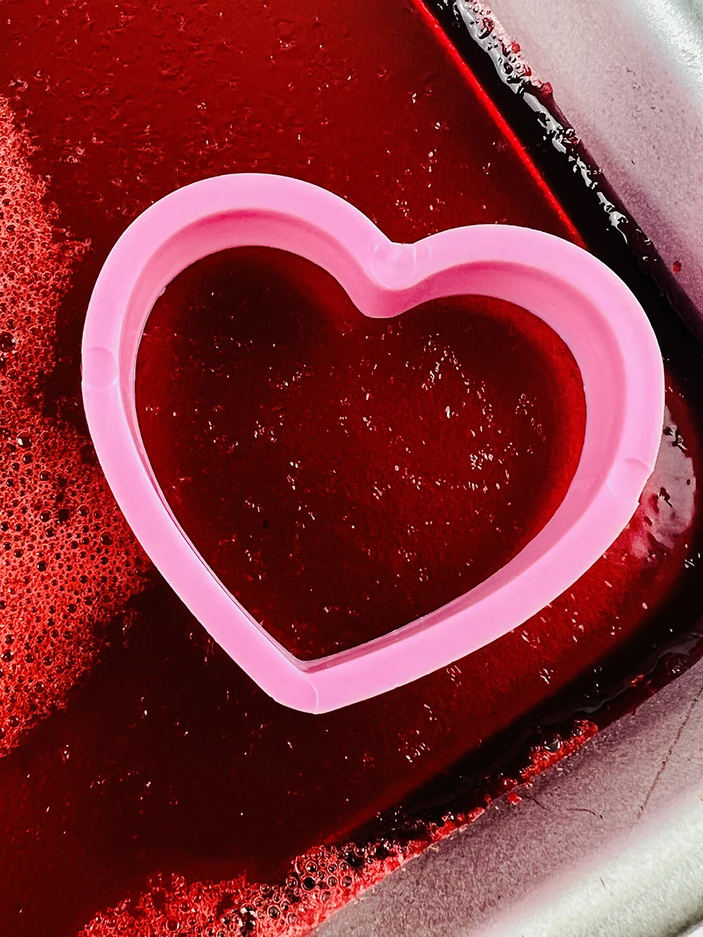 heart cookie cutter on a sheet of red jello