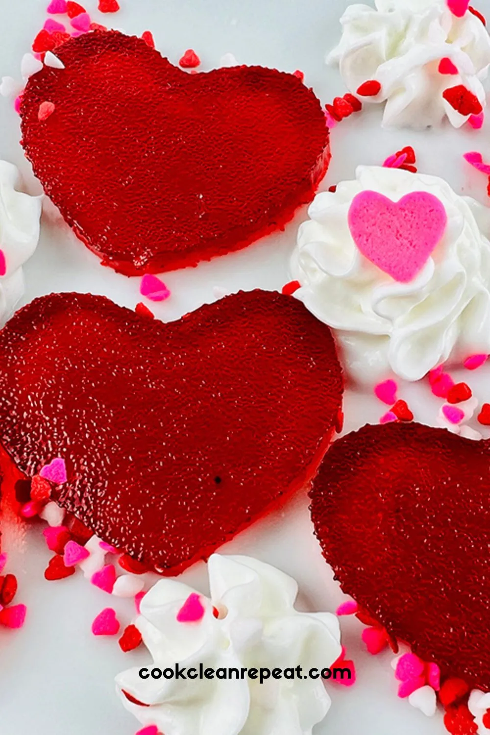 a close up of completed Valentine's Day jello jigglers on a white plate with sprinkles and whipped cream