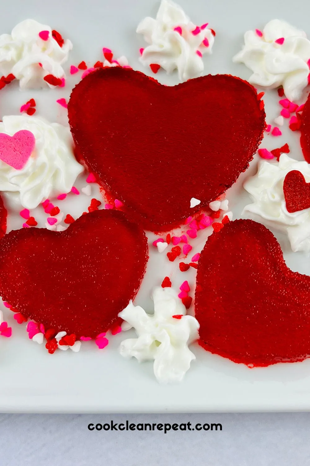 three completed Valentine's Day jello jigglers on a white plate with sprinkles and whipped cream