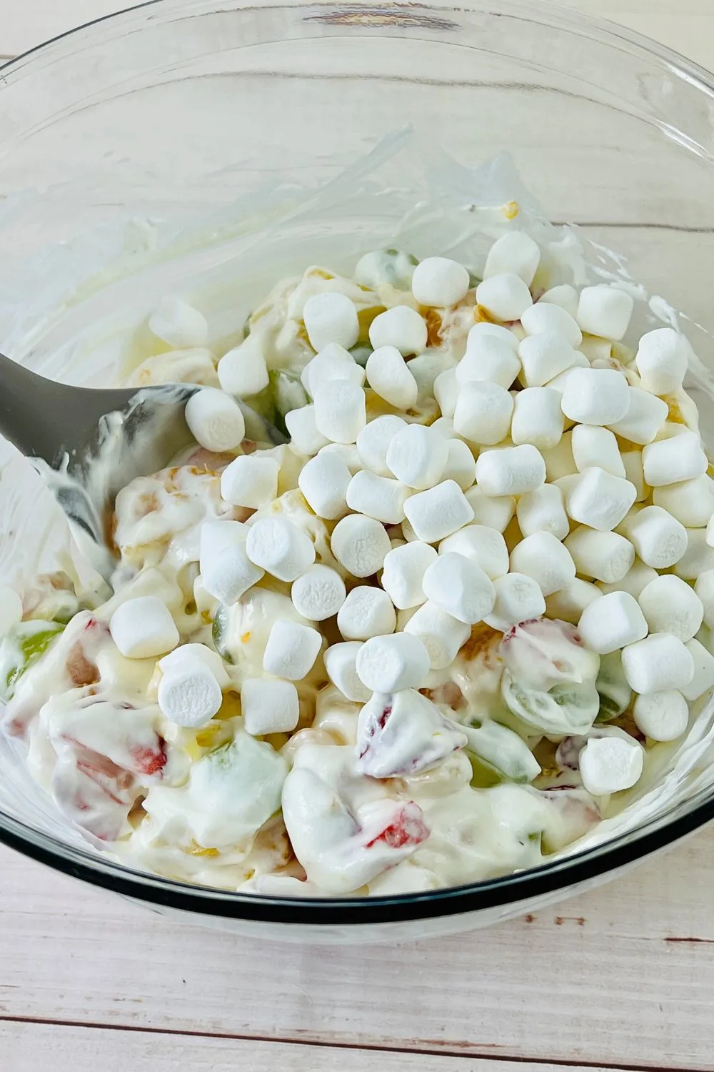 marshmallows being added to a fruit salad