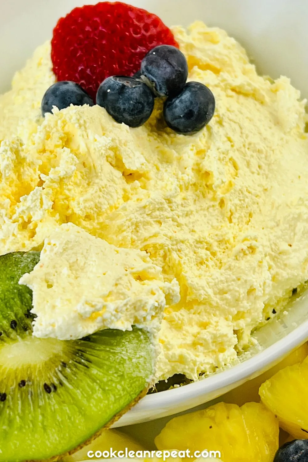 a bowl of cool whip fruit dip with different fruits around the bowl and on top of the dip.