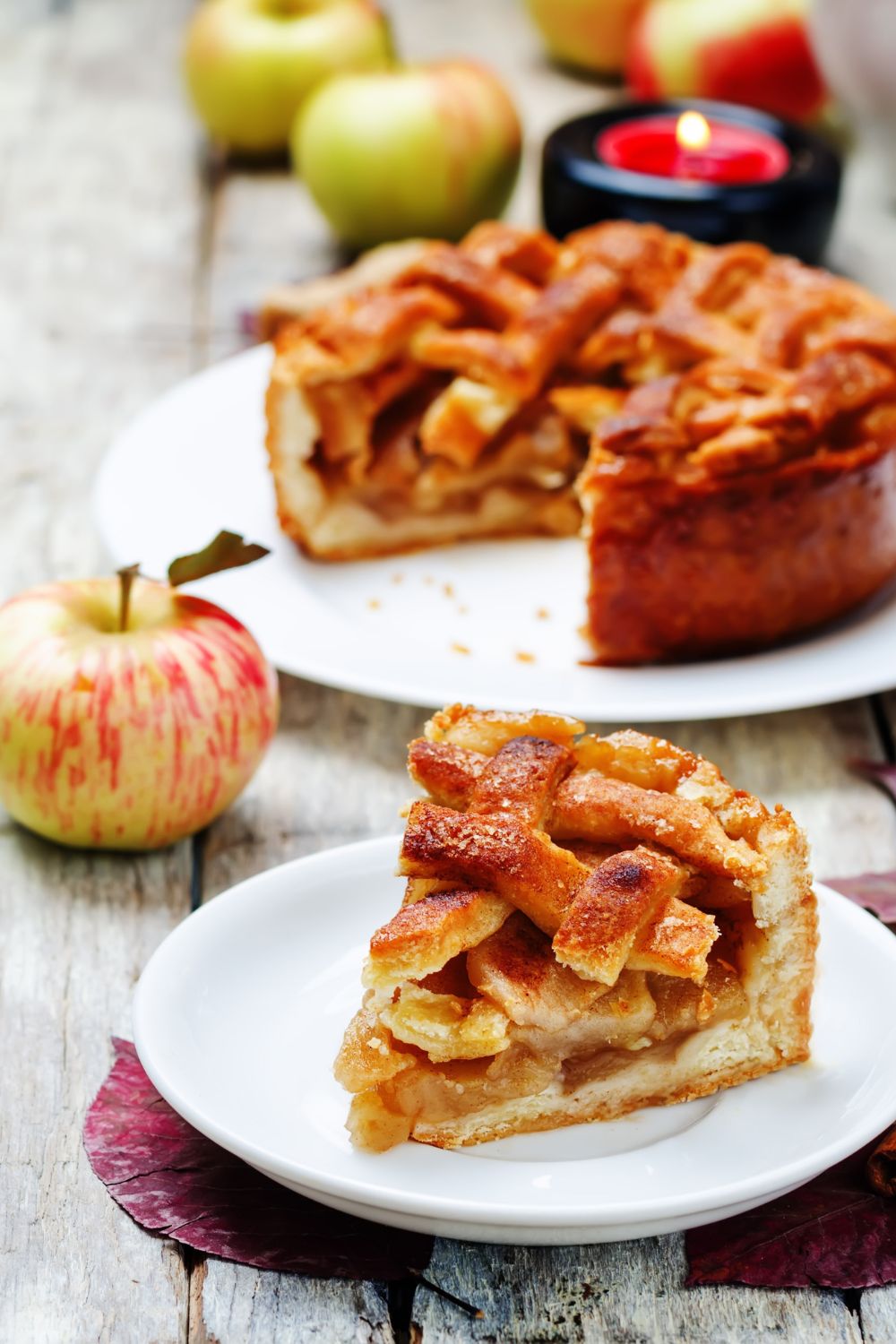 a slice of apple pie on a plate with the rest of the pie in the background
