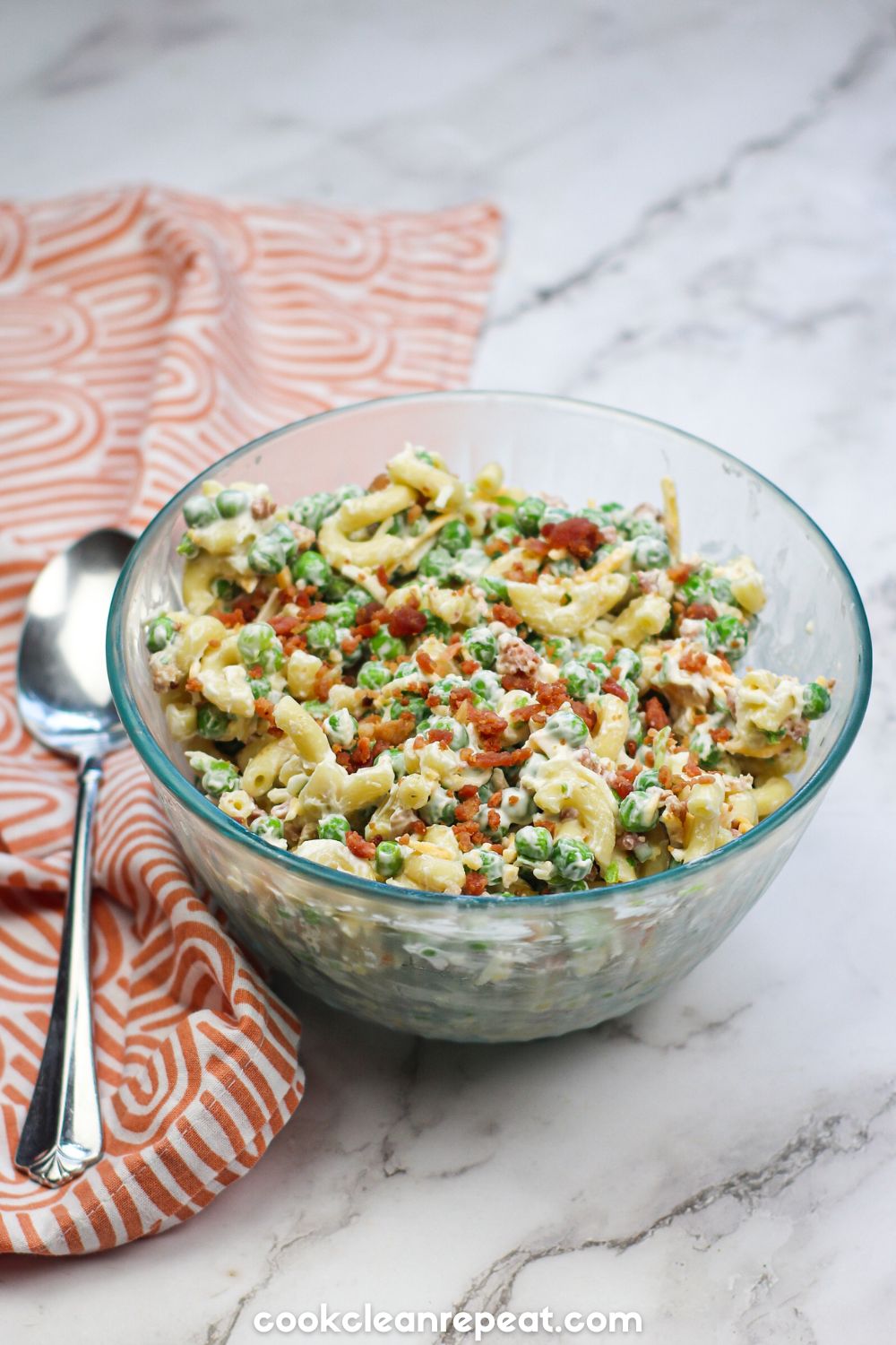 a bowl of pea and pasta salad on a marble background with a dish towel and spoon