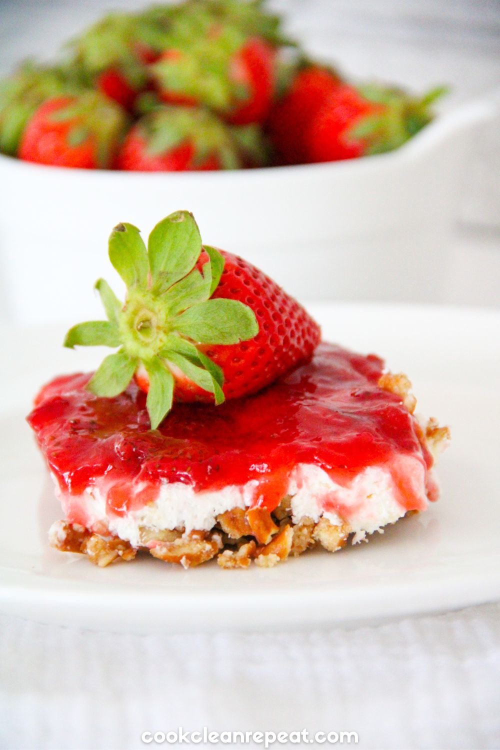 Strawberry Pretzel Salad slice served on a plate with bowl of strawberries in the background