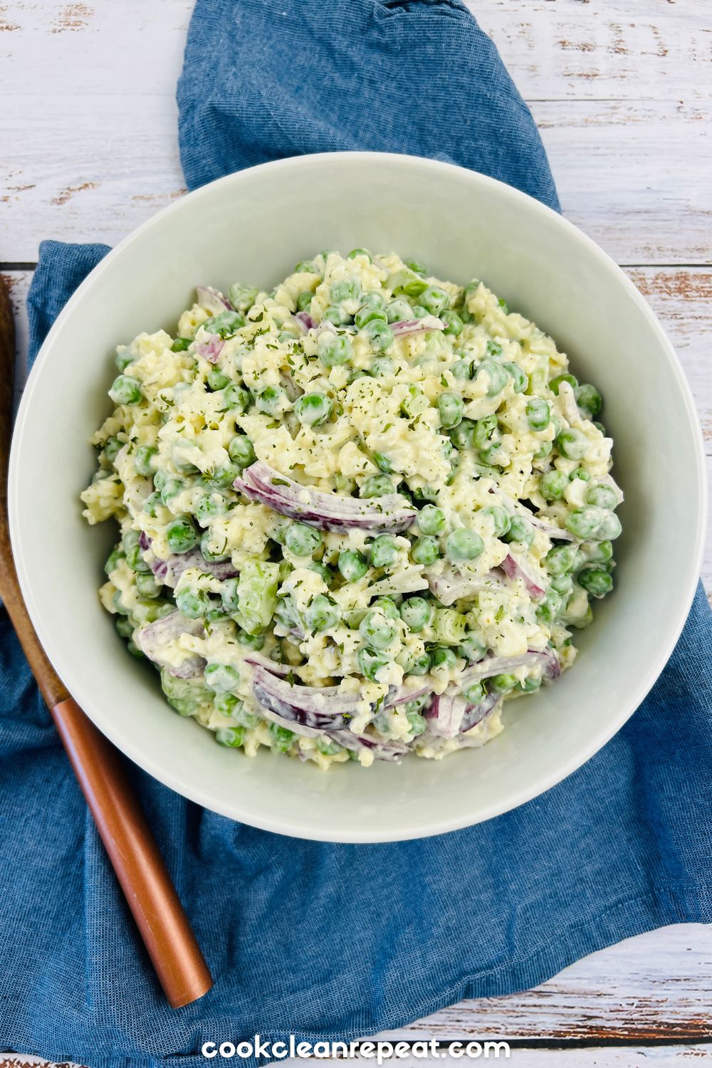 cauliflower pea salad in a bowl next to a wooden spoon