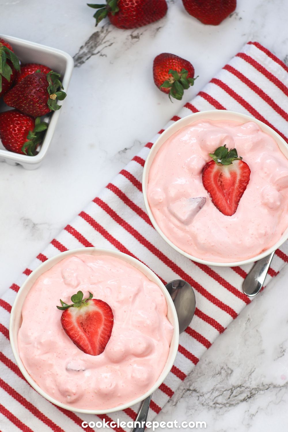 two bowls of strawberry fluff salad with strawberries around