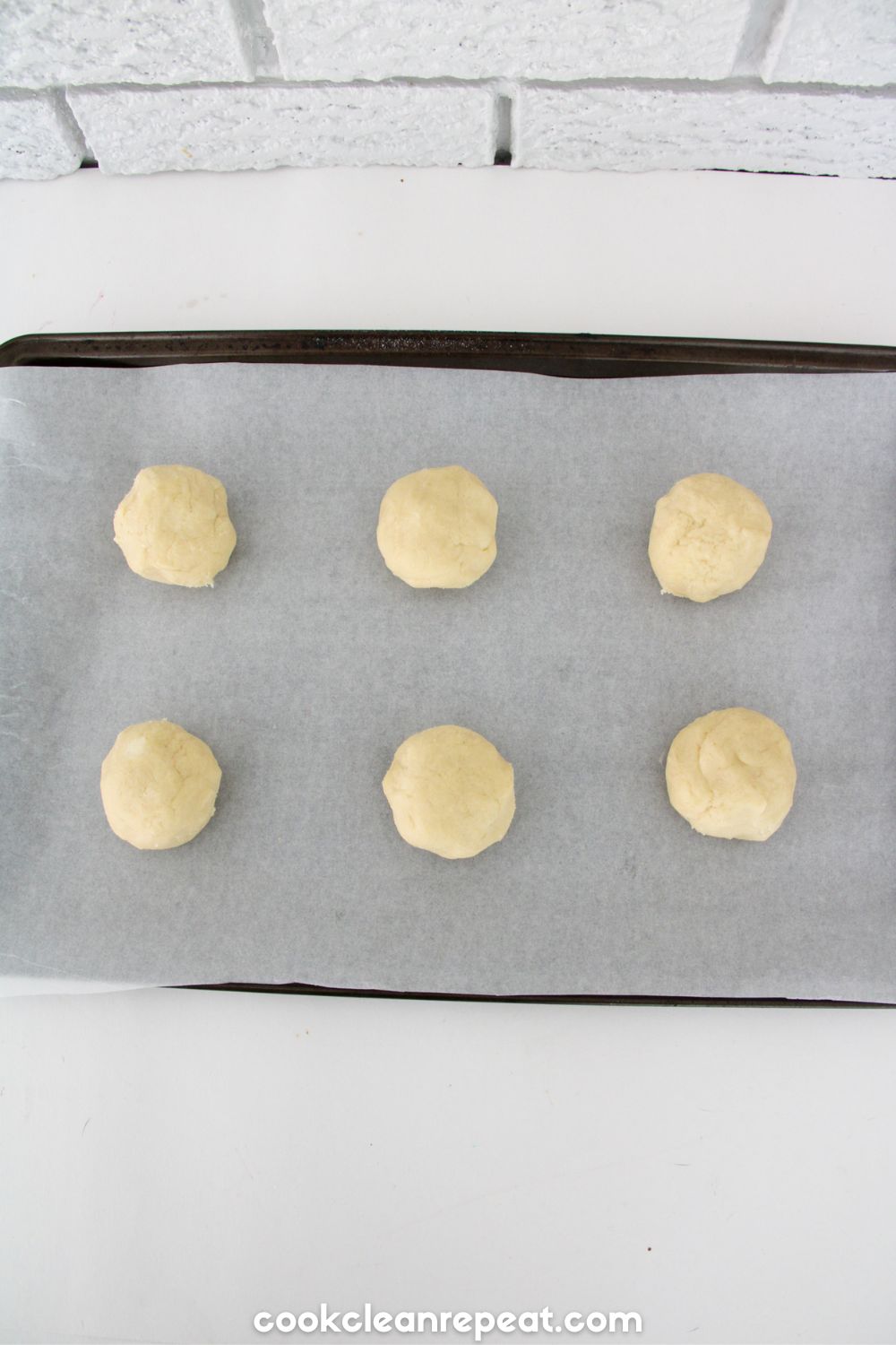 six balls of cookie dough on a parchment lined cookie sheet