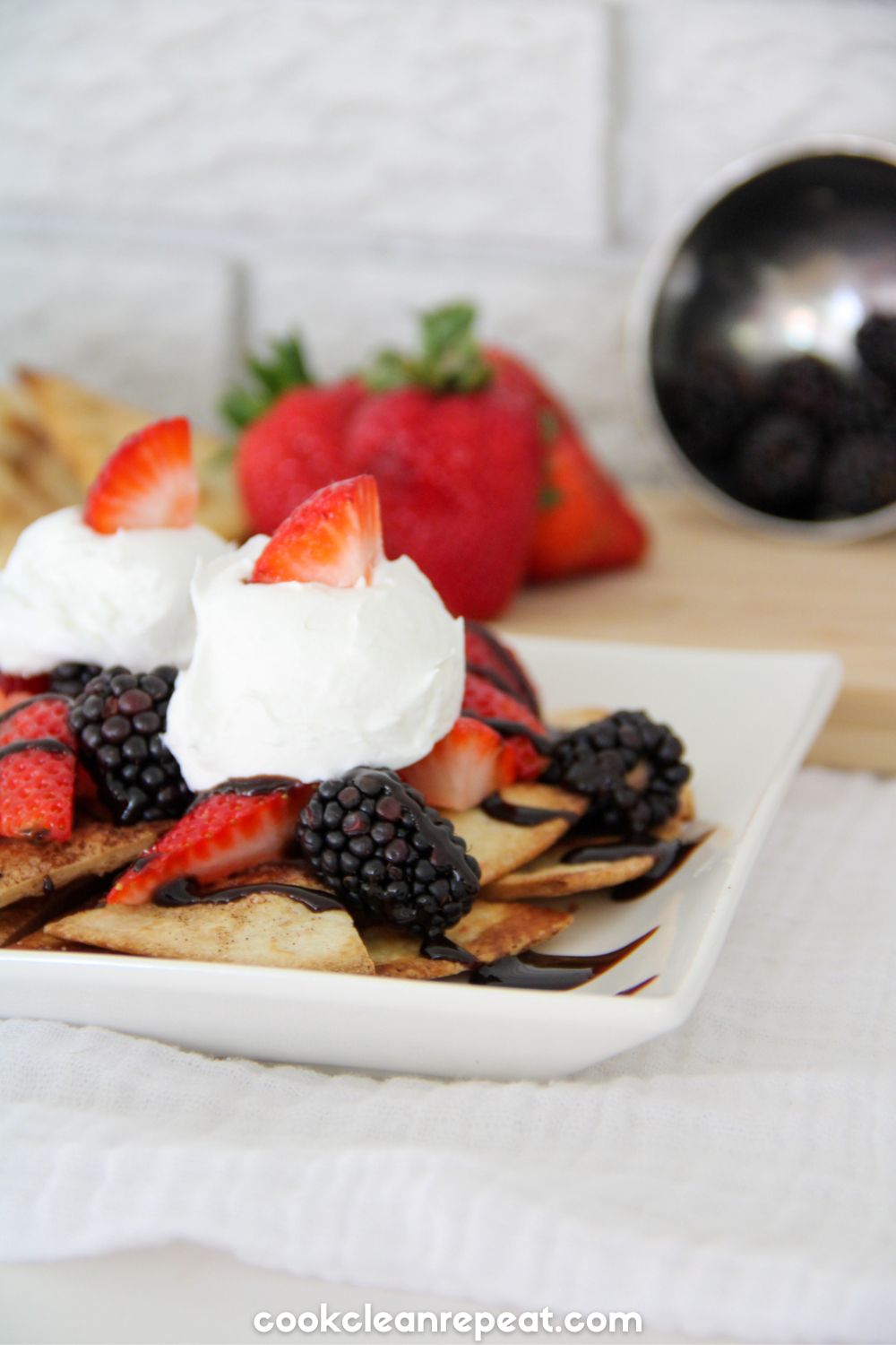 dessert nachos served on a white plate topped with whipped cream and strawberry pieces