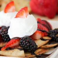 dessert nachos served on a white plate topped with whipped cream and strawberry pieces