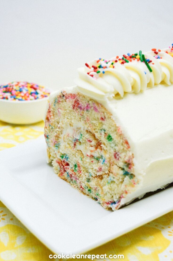 birthday cake roll sliced into with sprinkles beside it in a bowl
