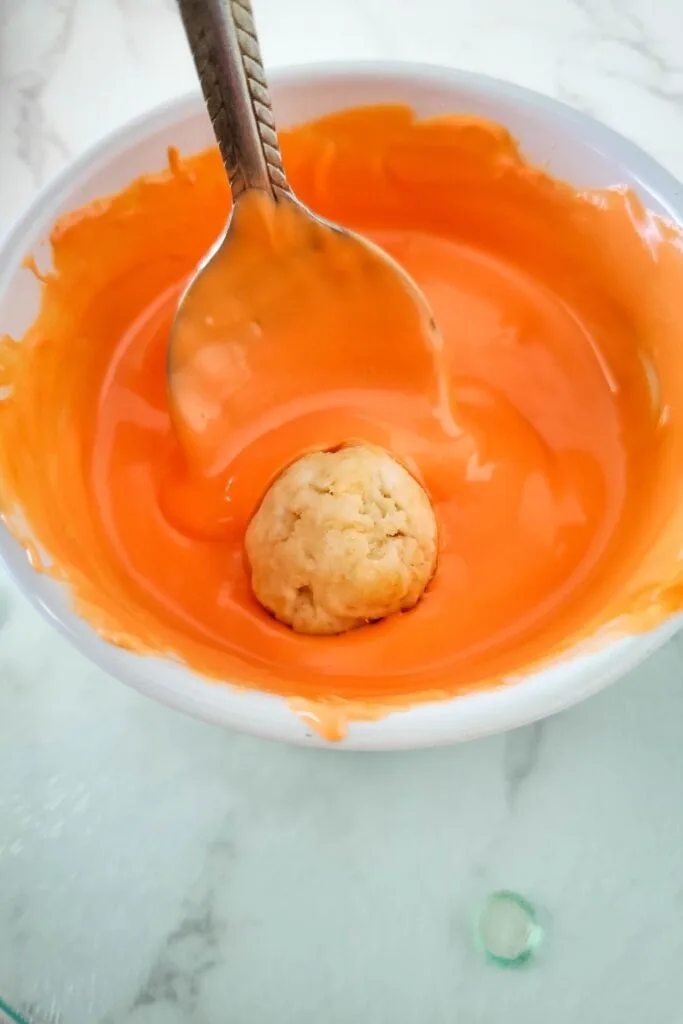 Thanksgiving Oreo Ball being dipped in orange candy melts