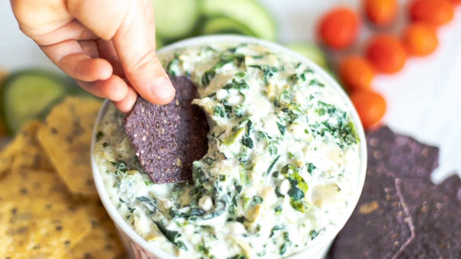 A bowl of spinach artichoke dip with a tortilla chip.
