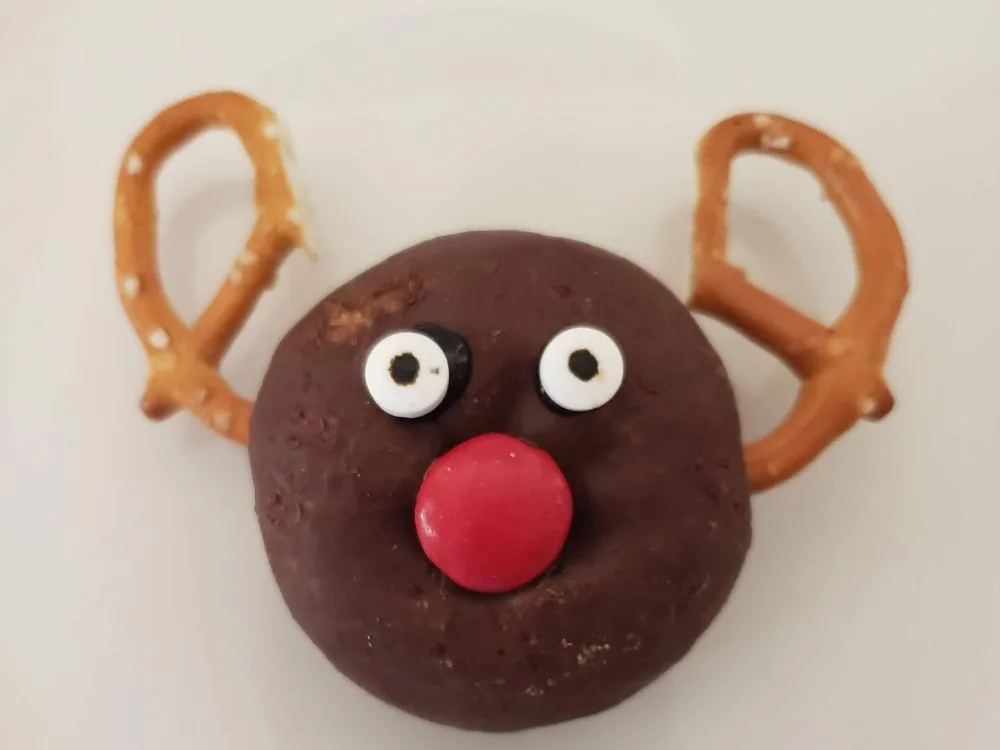 chocolate donut with pretzel antlers and eyeball sprinkles and red M&M for a nose