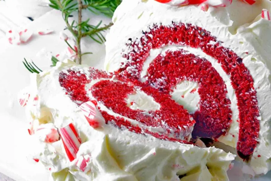  A red velvet cake roll with white frosting and candy canes crushed over the top.