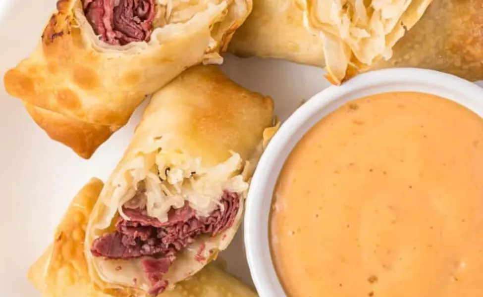 Egg rolls filled with cheese and corned beef, with dip on the side.