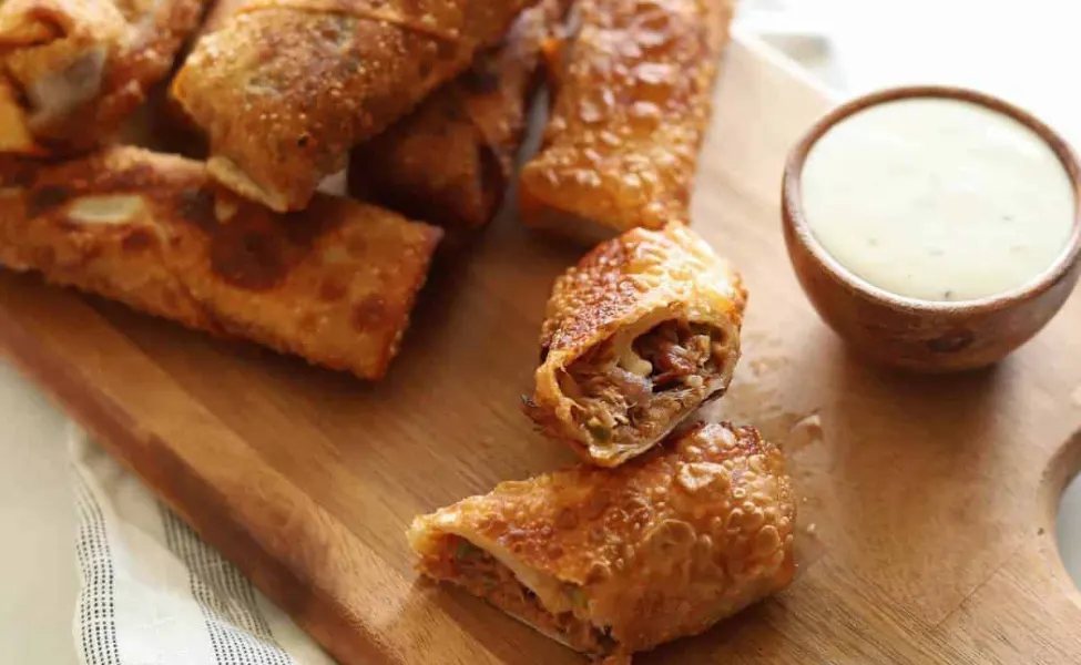 Egg rolls filled with bbq pulled pork on a cutting board.