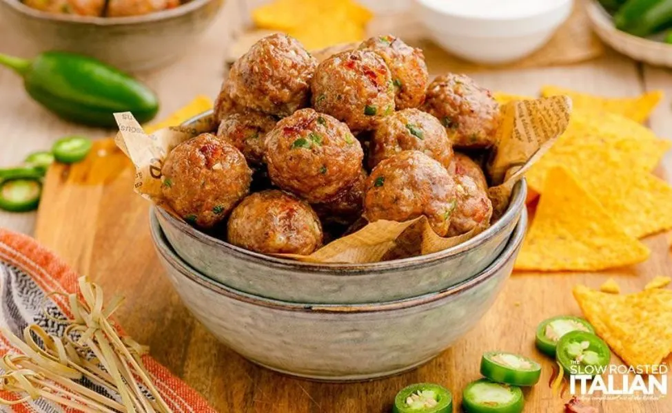 A bowl of meatballs with jalapeno peppers inside.
