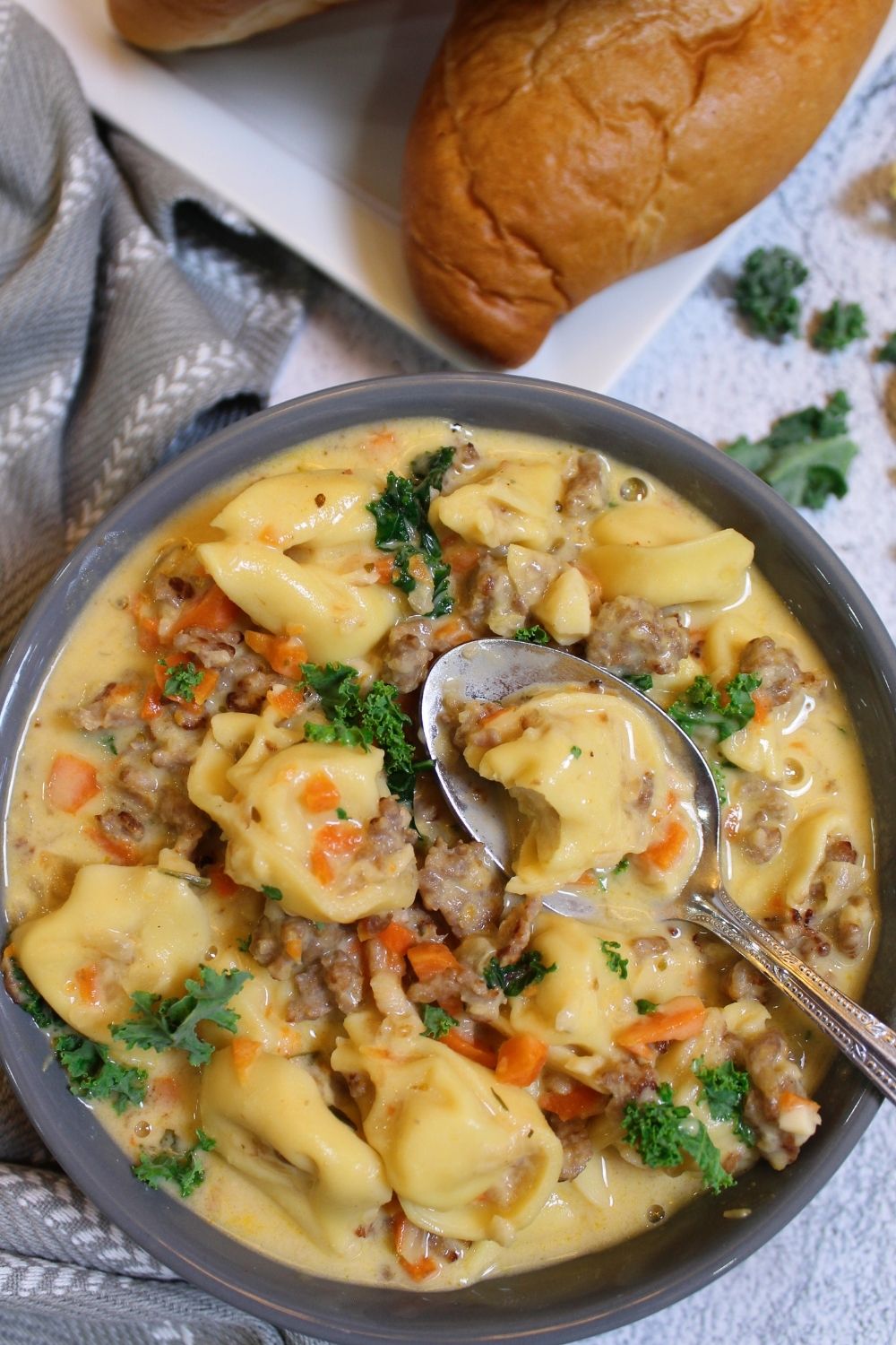 kale sausage tortellini soup in a bowl with rolls above