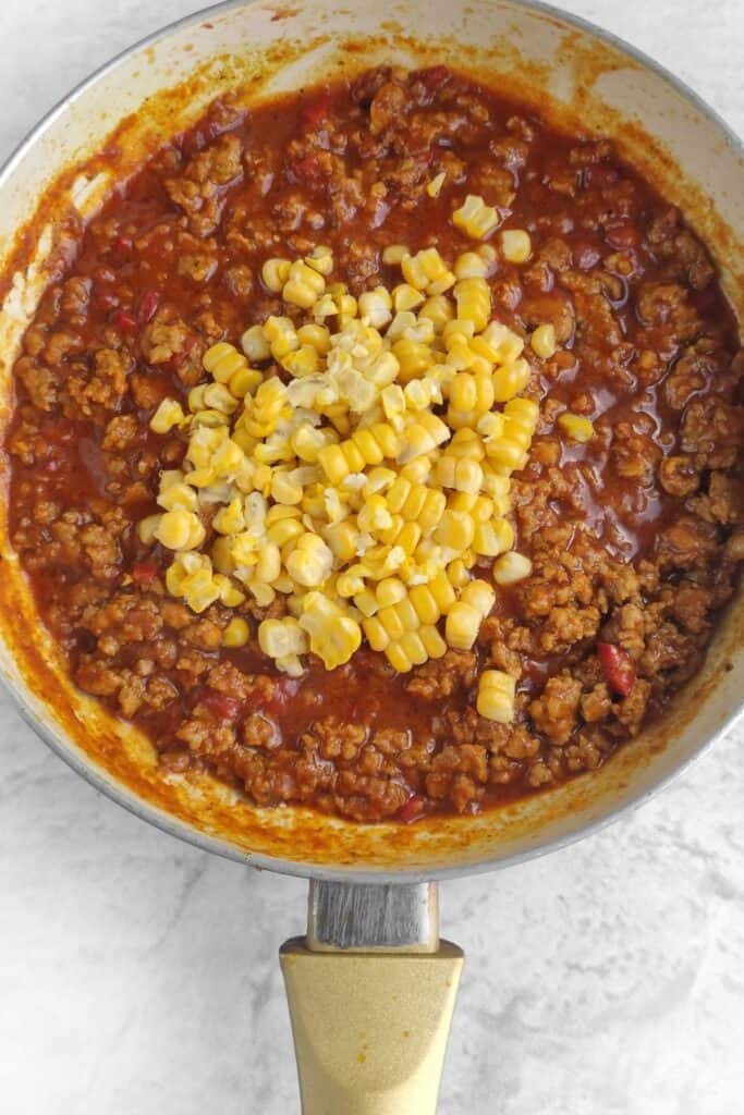 Corn being added to the meat and sauce.