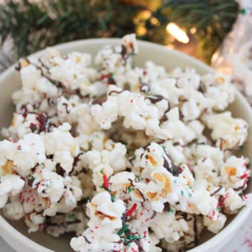 A bowl of Christmas popcorn with light decor in the background.