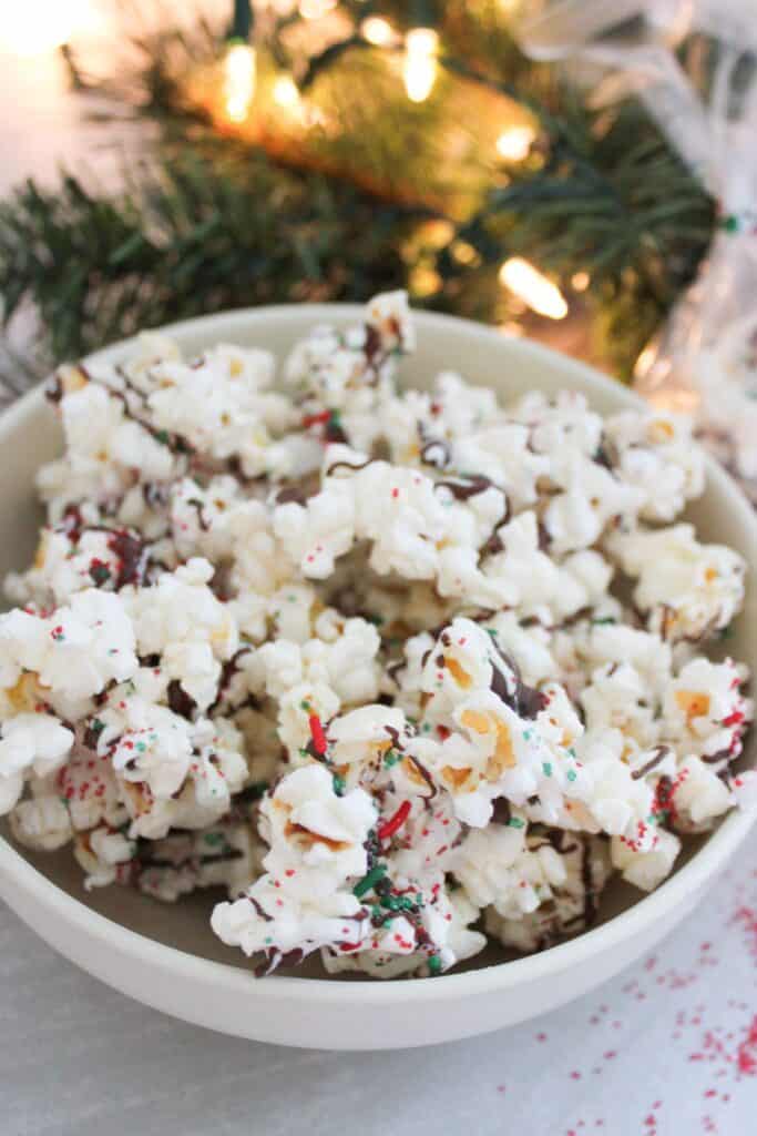 A bowl of Christmas popcorn with light decor in the background.