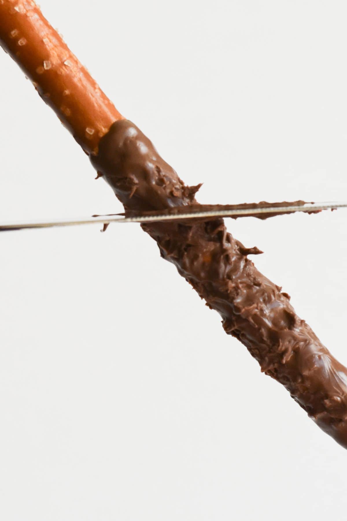 Adding texture to melted chocolate on a pretzel.